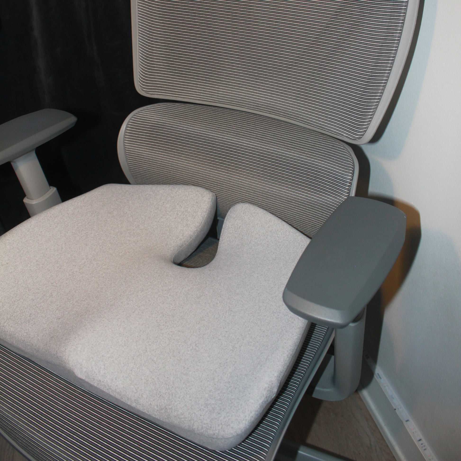 Ergonomisk memory foam siddepude i grå placeret på moderne kontorstol med armlæn. Giver støtte og aflaster ryg og hofter under lange arbejdsdage. Copenhagen Comfort.