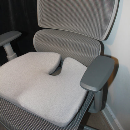 Ergonomisk memory foam siddepude i grå placeret på moderne kontorstol med armlæn. Giver støtte og aflaster ryg og hofter under lange arbejdsdage. Copenhagen Comfort.