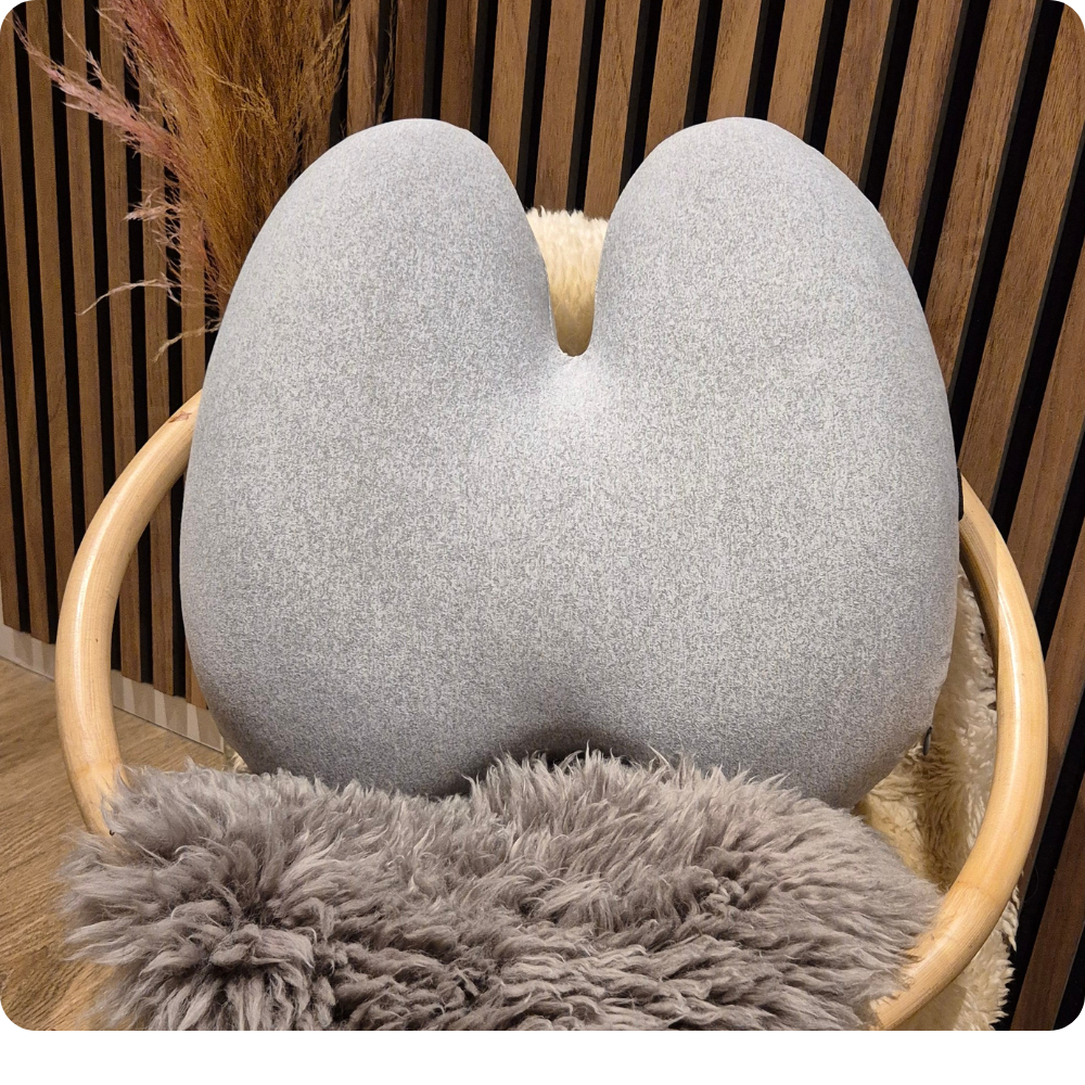 Ergonomisk memory foam rygpude i grå fra Copenhagen Comfort, placeret på stol med blødt pelsunderlag. Aflaster ryg og giver støtte i hjemmet