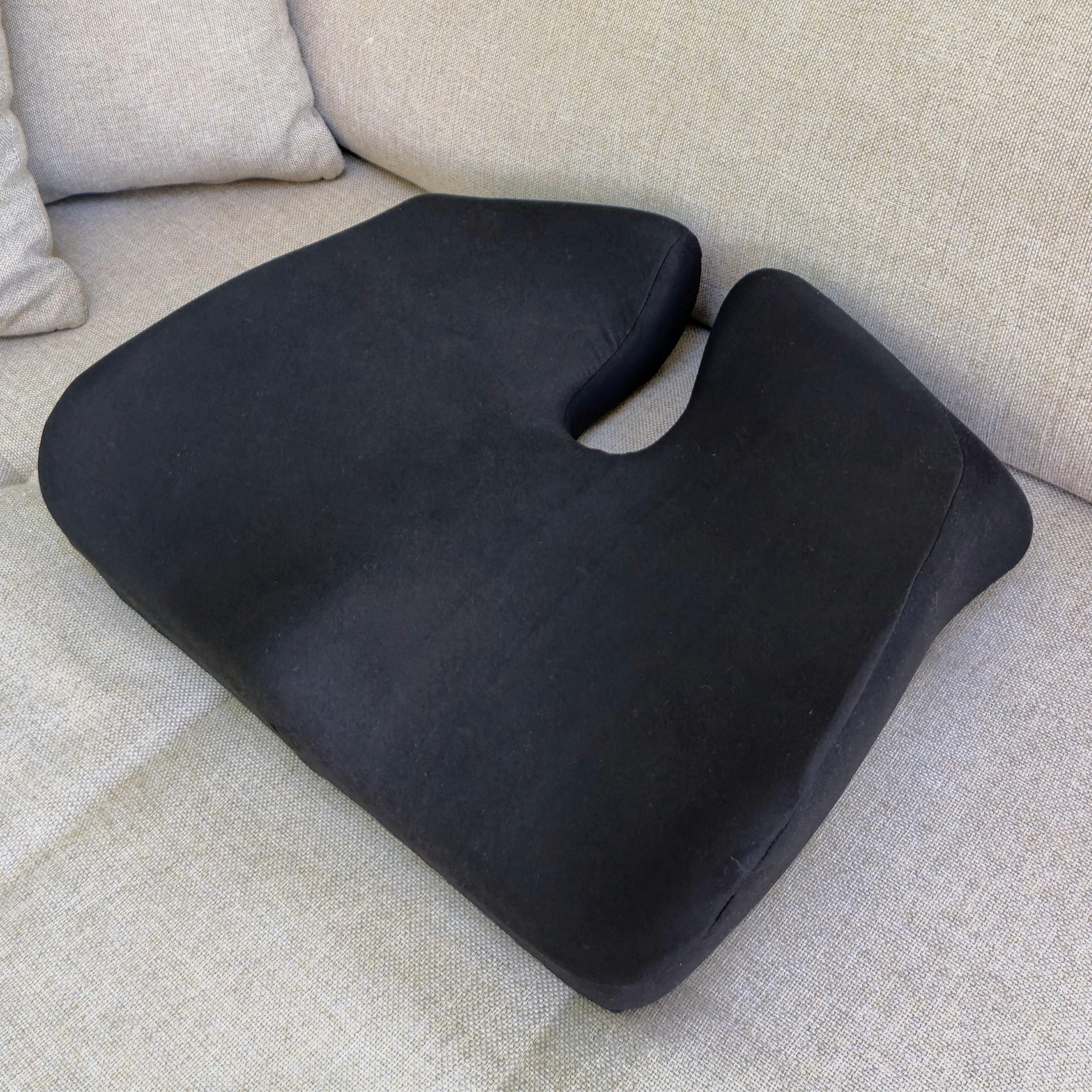 Sort ergonomisk memory foam siddepude placeret i sofa, designet til at aflaste ryg og hofter. Copenhagen Comforts pude giver støtte og komfort i hjemmet.