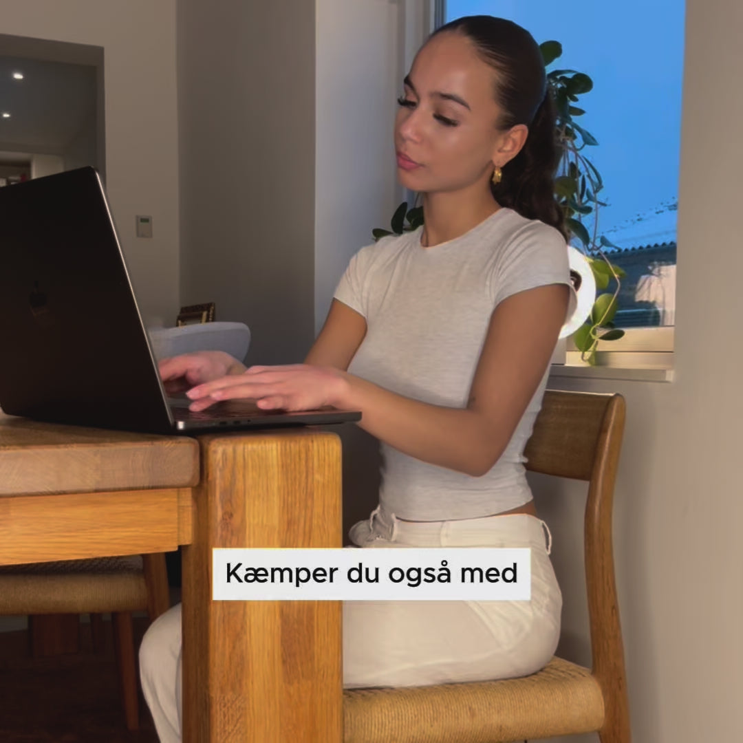 Indlæs video: Kvinde arbejder ved laptop med ergonomisk memory foam siddepude fra Copenhagen Comfort, der giver støtte og komfort under længere tids siddestilling